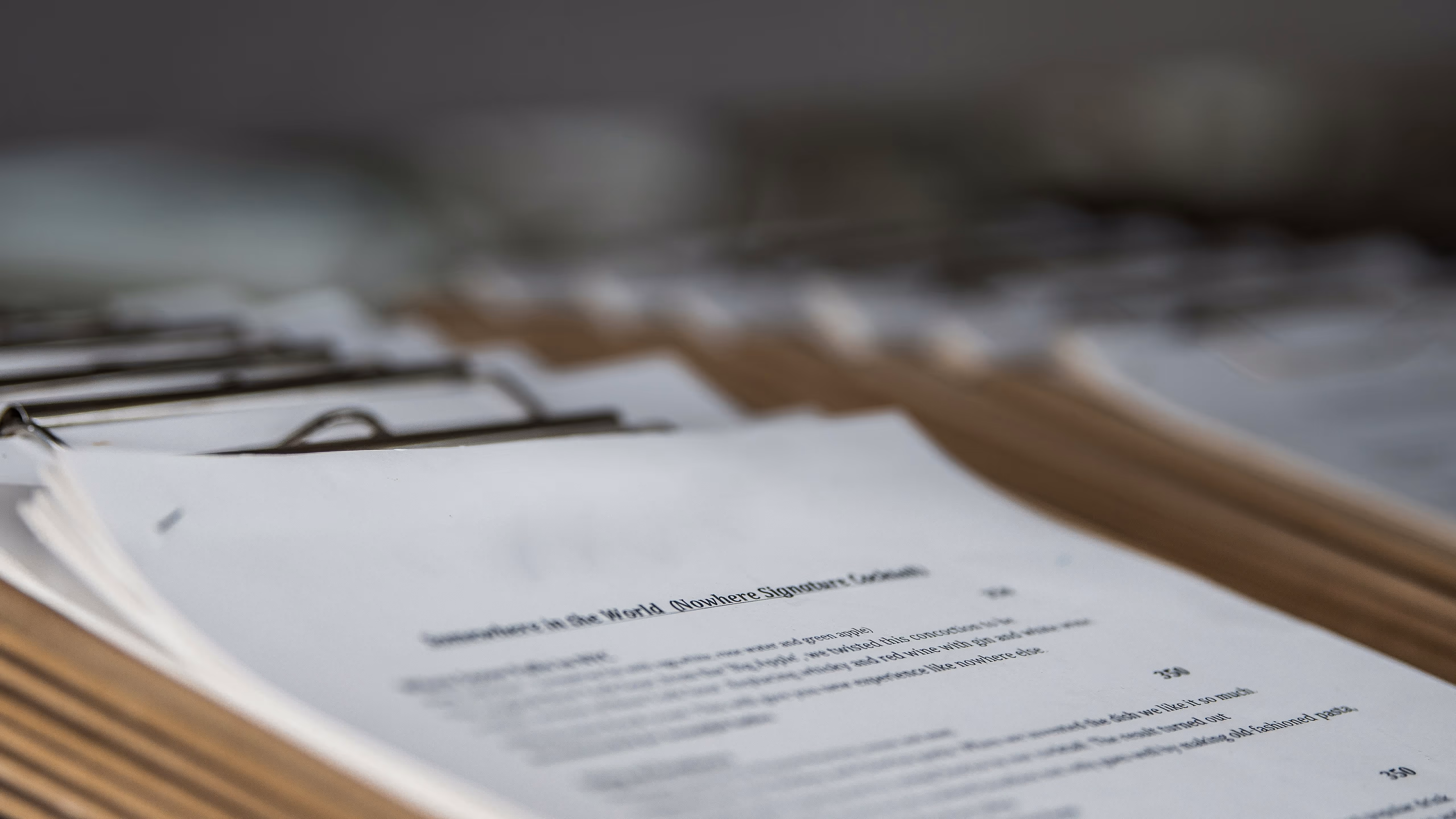 Close-up of a document on a wooden surface with blurred text and other papers in the background.
